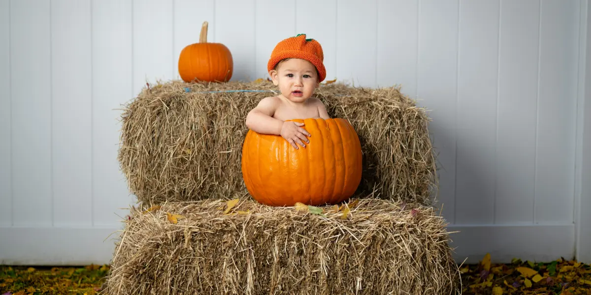 Baby in a pumpkin on a stack of hay.