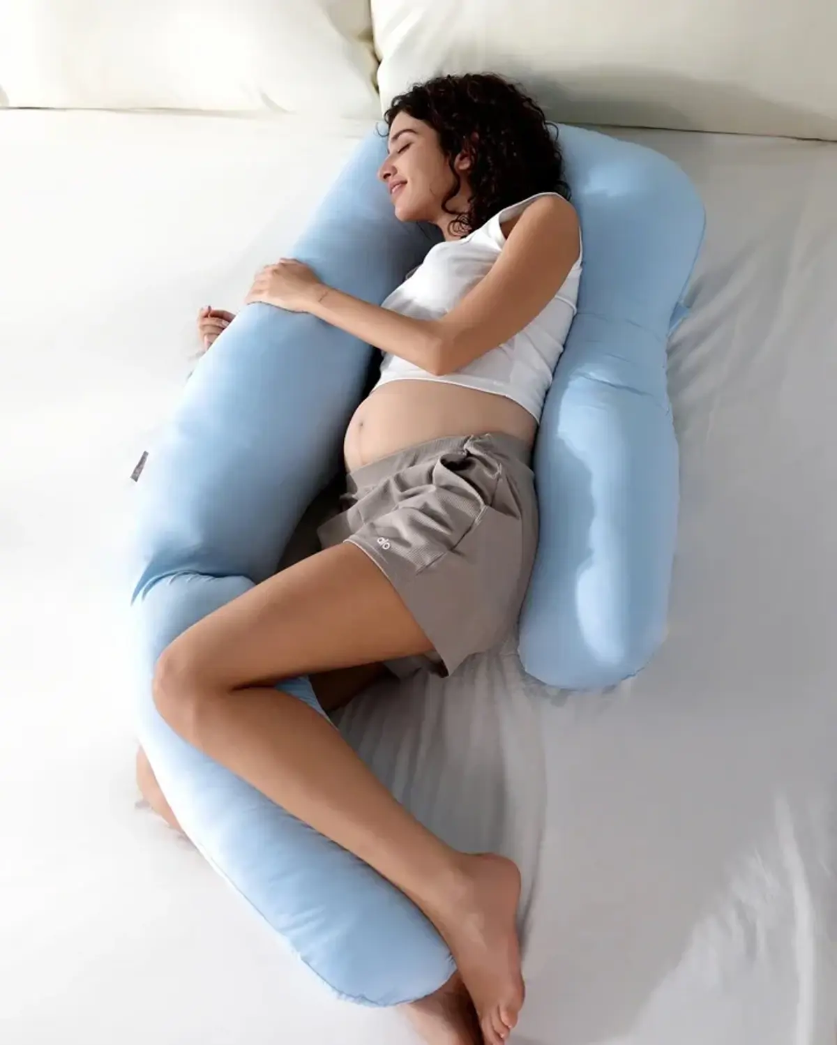 A blue U-shaped pregnancy support pillow on a bed