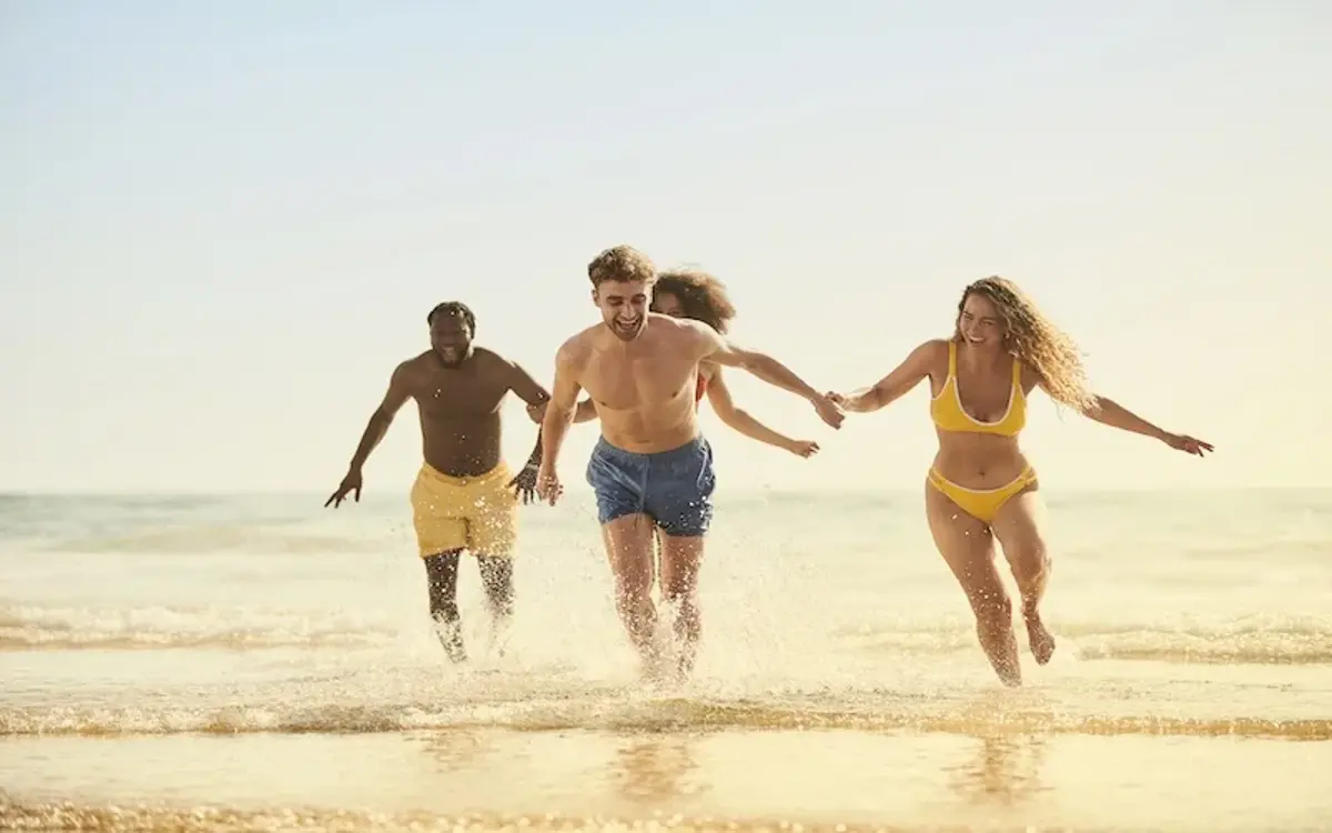 Three friends running out of the sea laughing