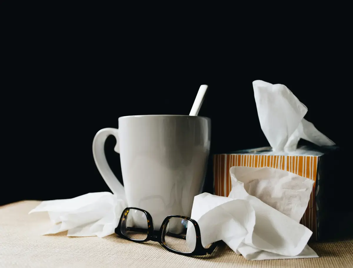 A mug, glasses and used tissues on a sick-day table