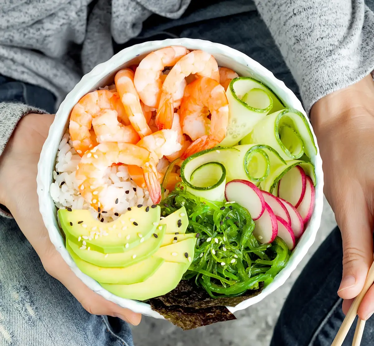 A prawn and avocado poke bowl held in two hands