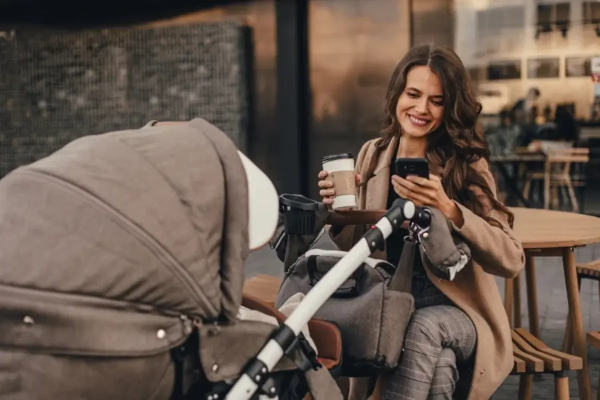 A mum with a pram checking her phone over coffee
