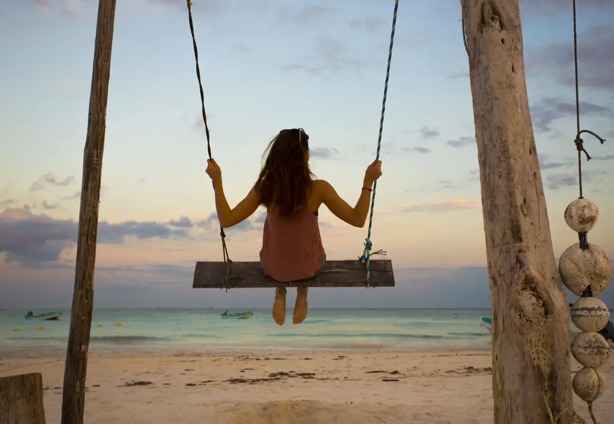 A woman on a beach swing at sunset