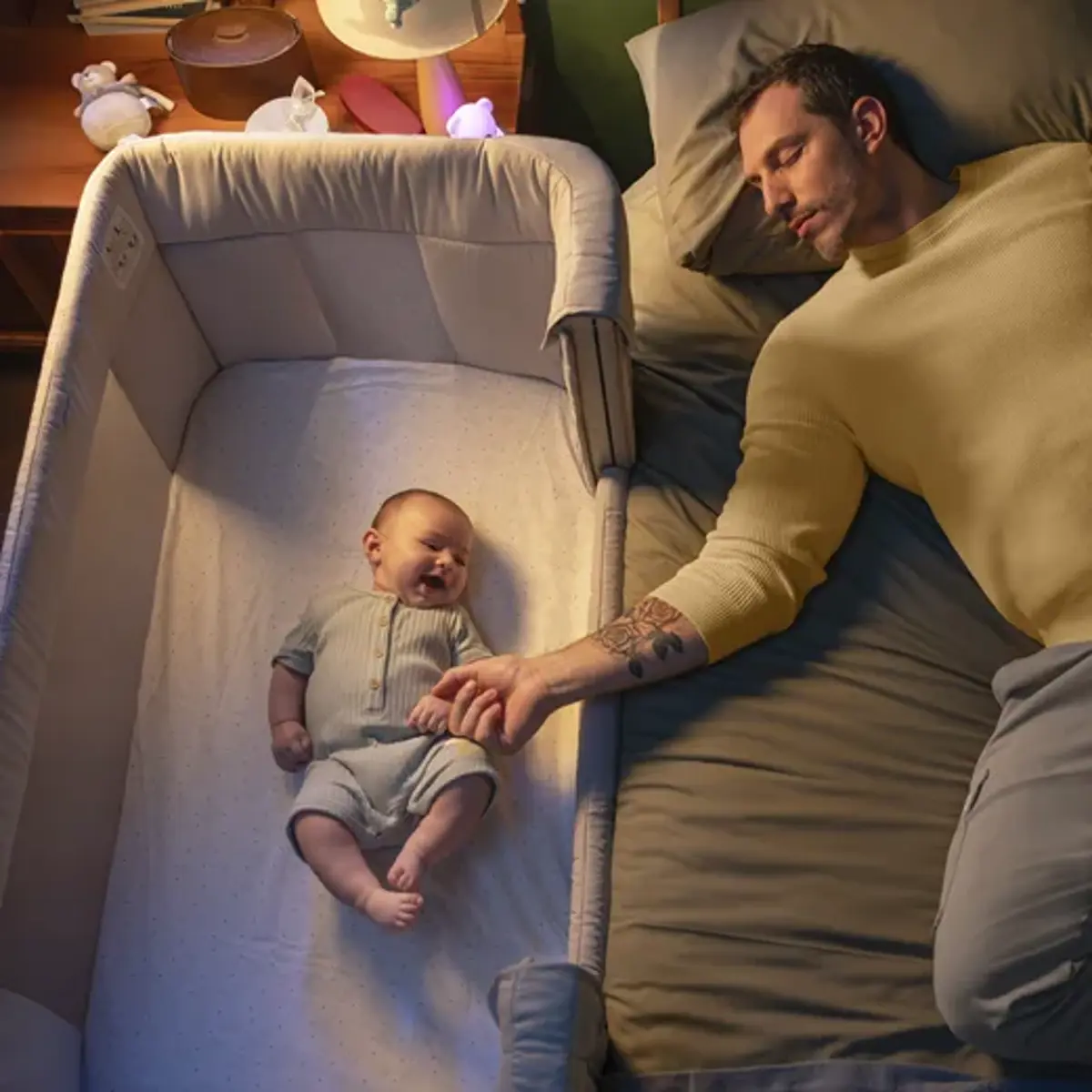 A dad asleep beside his baby's bedside crib