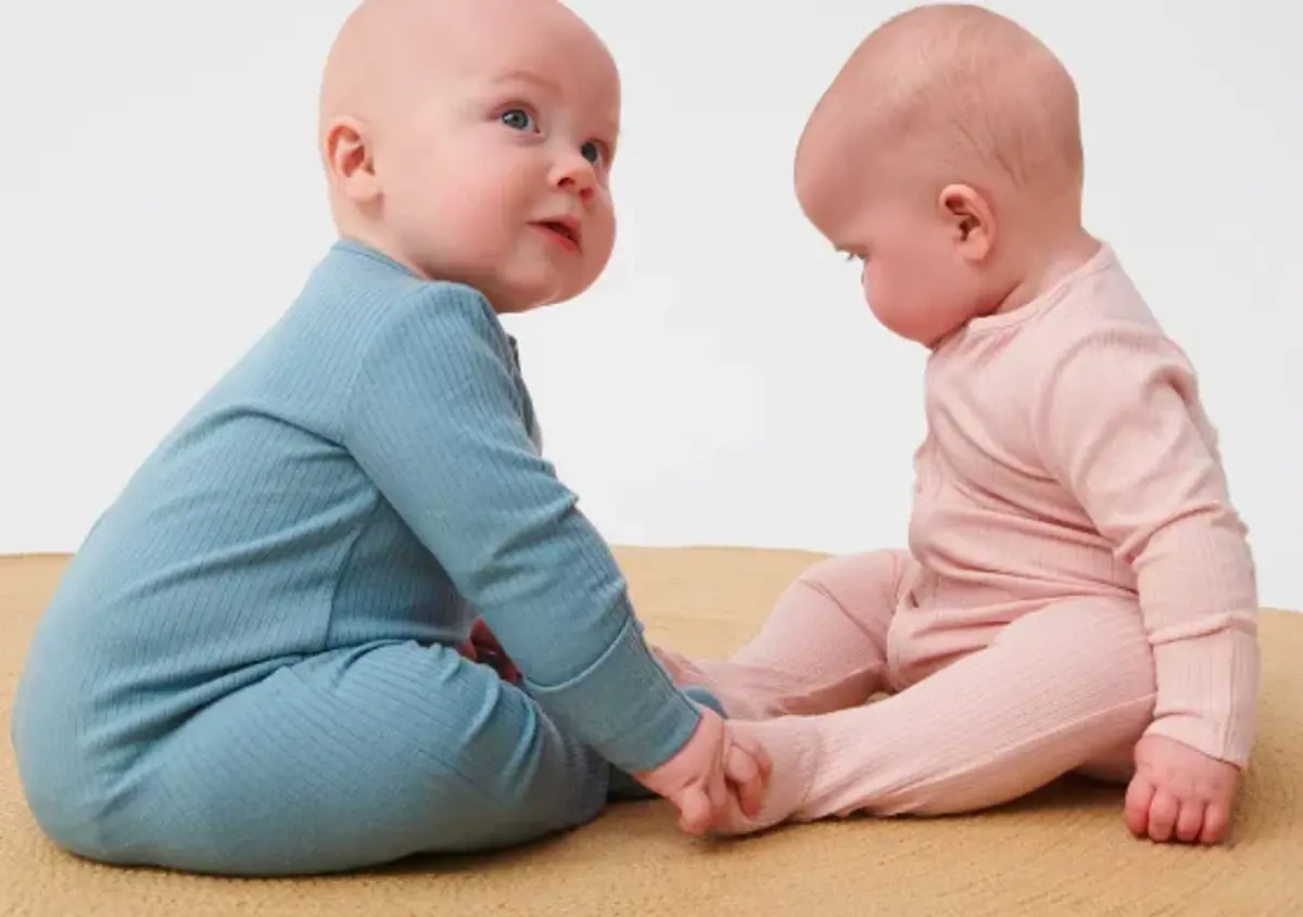 Two babies in blue and pink sitting face to face