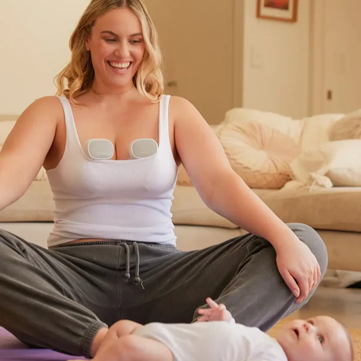 A mum using a wearable breast pump while sitting with her baby